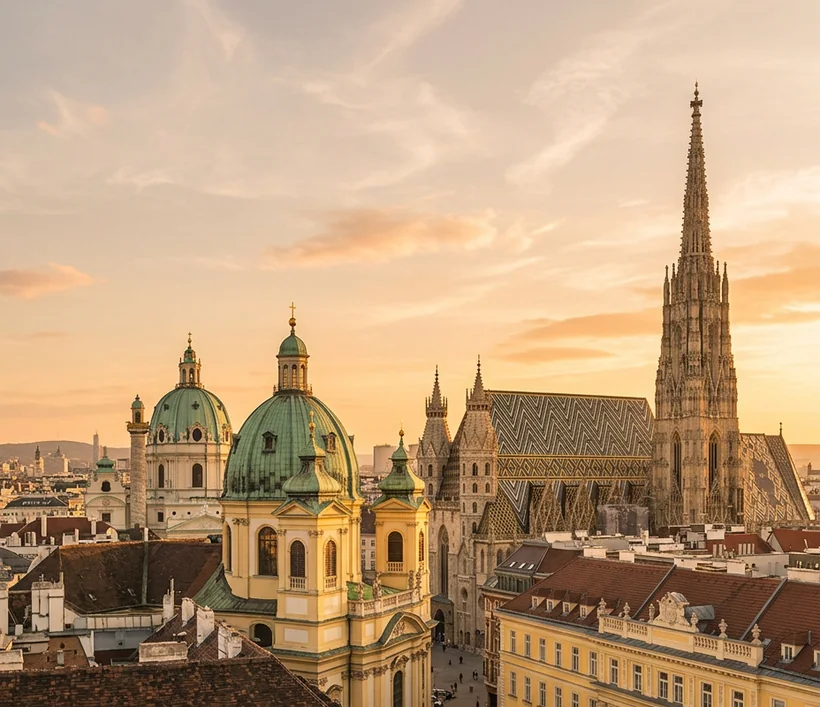 Vienna skyline at golden hour with baroque green domes and the Gothic spire of St. Stephen's Cathedral above ochre palace façades